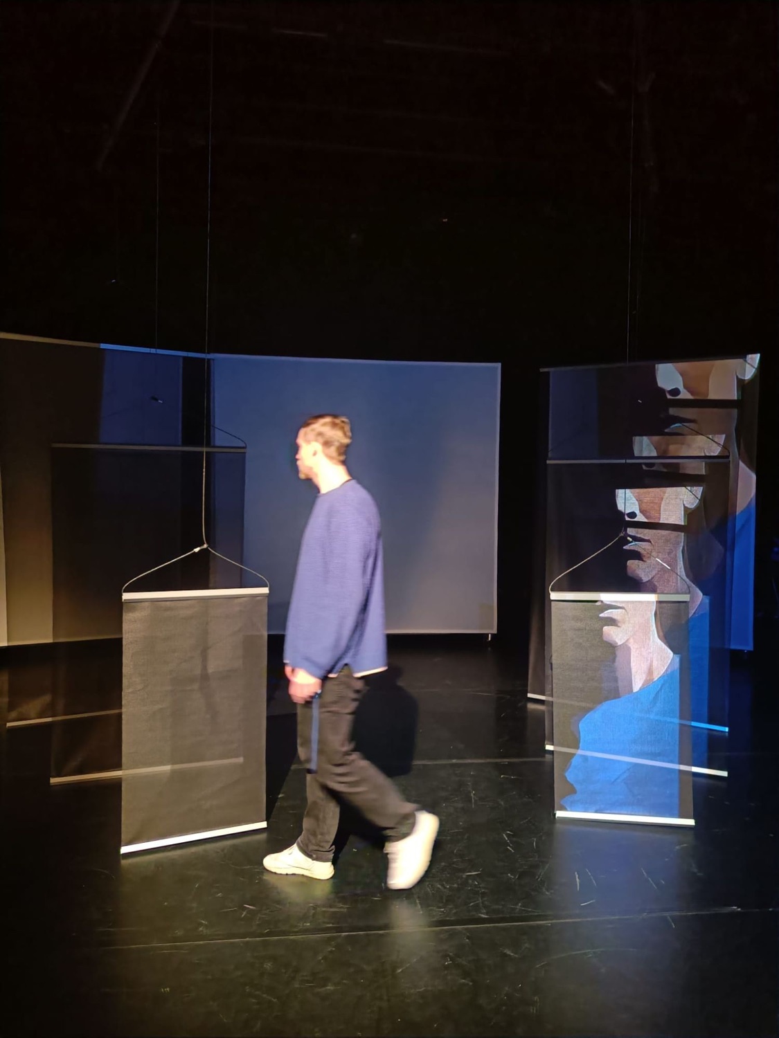 Antti Uimonen walking between hanging screens showing a fragmented, AI-generated silhouette portrait.